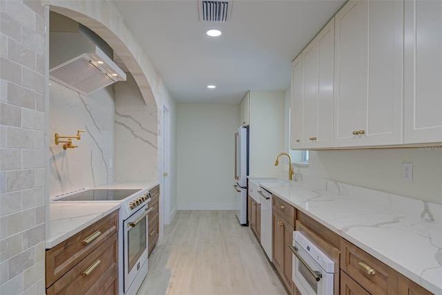 kitchen with light stone counters, high end appliances, wall chimney exhaust hood, white cabinetry, and visible vents