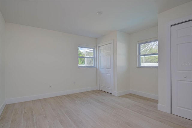 unfurnished bedroom featuring baseboards, multiple windows, and light wood-style flooring