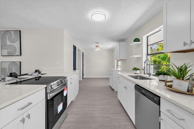 kitchen featuring light countertops, appliances with stainless steel finishes, white cabinetry, a sink, and open shelves