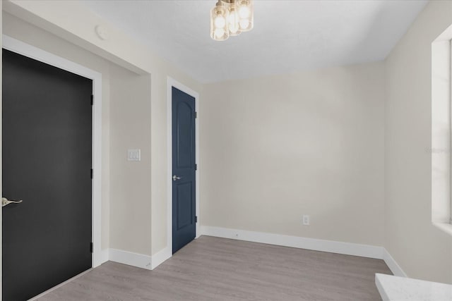 unfurnished room featuring baseboards, an inviting chandelier, and light wood-style floors