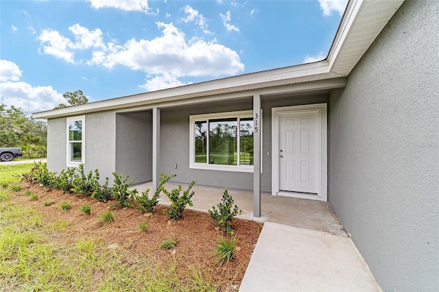 doorway to property with stucco siding and covered porch