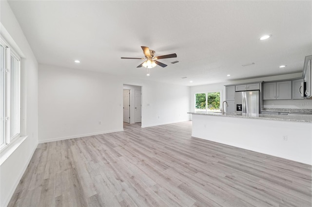 unfurnished living room featuring light wood finished floors, visible vents, baseboards, a ceiling fan, and a sink