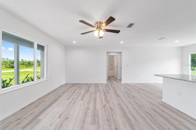 unfurnished living room with light wood-style flooring, plenty of natural light, a ceiling fan, and visible vents