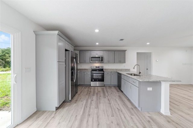 kitchen featuring gray cabinetry, light wood-style flooring, appliances with stainless steel finishes, a peninsula, and a sink