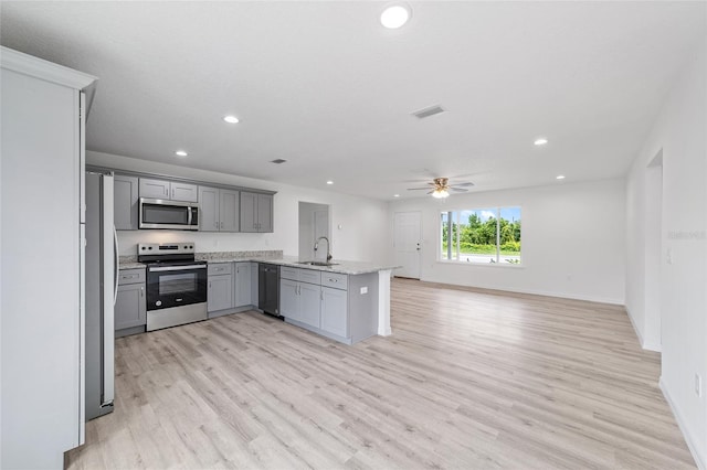 kitchen with gray cabinetry, ceiling fan, open floor plan, appliances with stainless steel finishes, and a sink