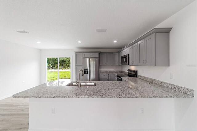 kitchen featuring light stone countertops, a peninsula, gray cabinets, a sink, and appliances with stainless steel finishes