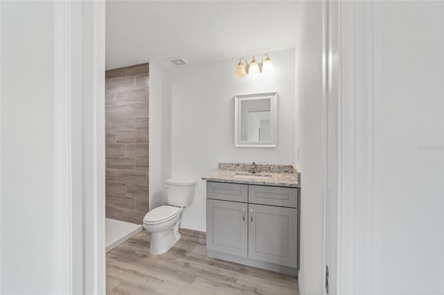 bathroom with vanity, wood finished floors, a tile shower, a textured ceiling, and toilet
