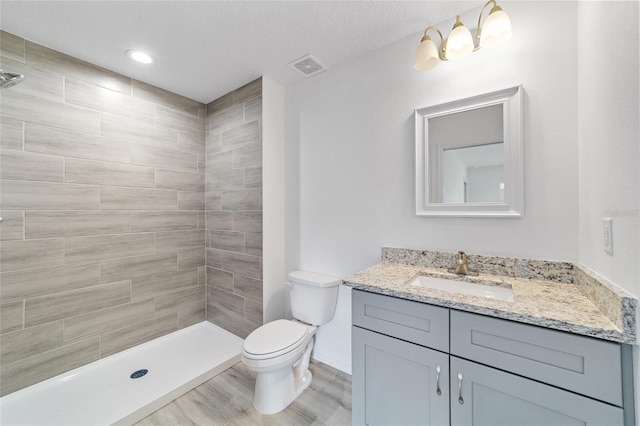 full bathroom featuring visible vents, toilet, tiled shower, wood finished floors, and vanity