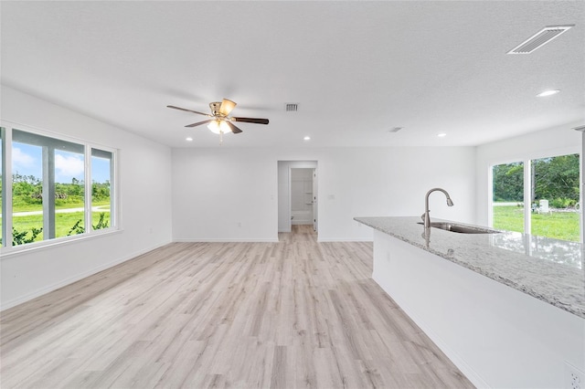unfurnished living room featuring a sink, visible vents, plenty of natural light, and light wood-type flooring