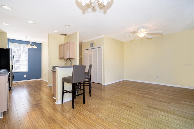 6274 Bristol Channel Way, Orlando, FL 32829 - kitchen with light wood finished floors, a kitchen bar, ceiling fan with notable chandelier, freestanding refrigerator, and a sink