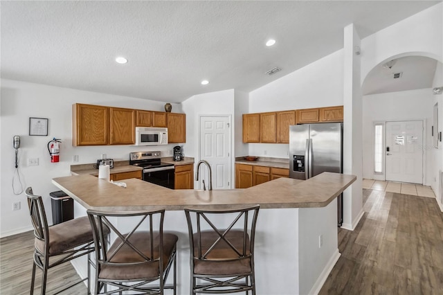 kitchen featuring wood finished floors, brown cabinetry, stainless steel appliances, visible vents, and arched walkways