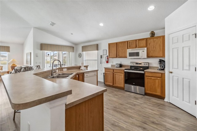 kitchen with lofted ceiling, light wood-type flooring, white appliances, a sink, and a large island