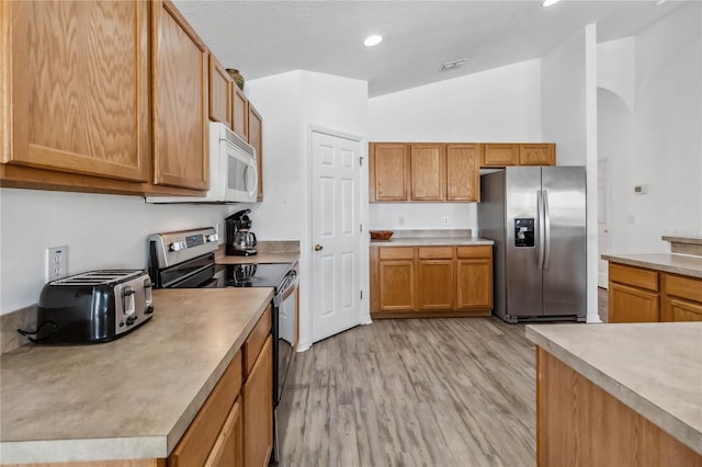 kitchen with light countertops, lofted ceiling, stainless steel appliances, visible vents, and light wood-style floors