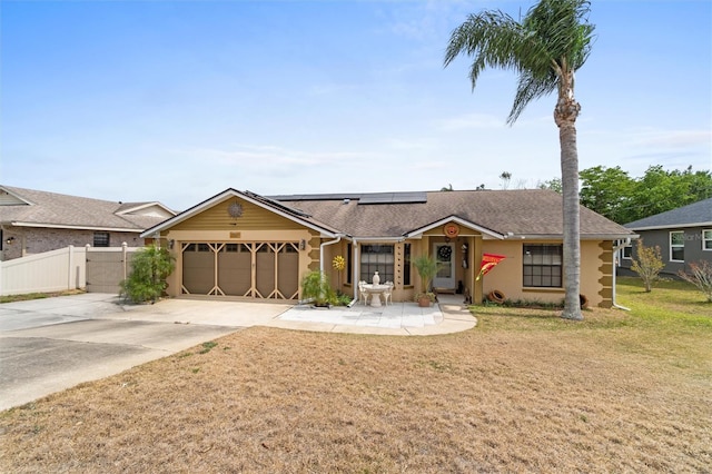 ranch-style house with driveway, a front yard, fence, an attached garage, and roof mounted solar panels