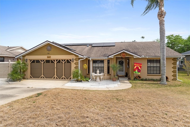 single story home with roof mounted solar panels, a front yard, a garage, and concrete driveway