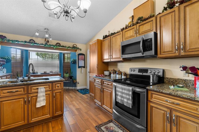 kitchen with a notable chandelier, a sink, appliances with stainless steel finishes, brown cabinetry, and visible vents