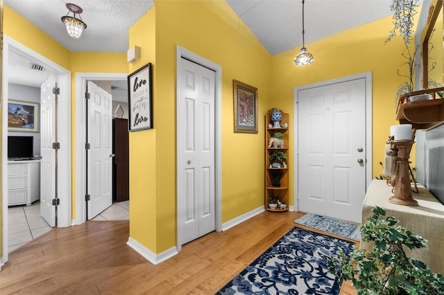foyer with visible vents, a textured ceiling, baseboards, and light wood-type flooring