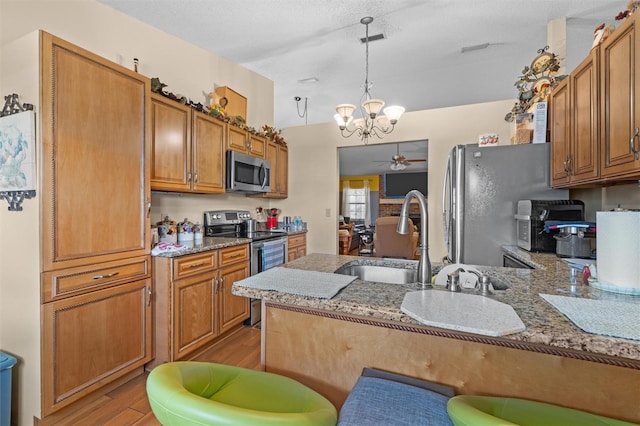 kitchen with stainless steel appliances, brown cabinetry, a peninsula, and ceiling fan with notable chandelier