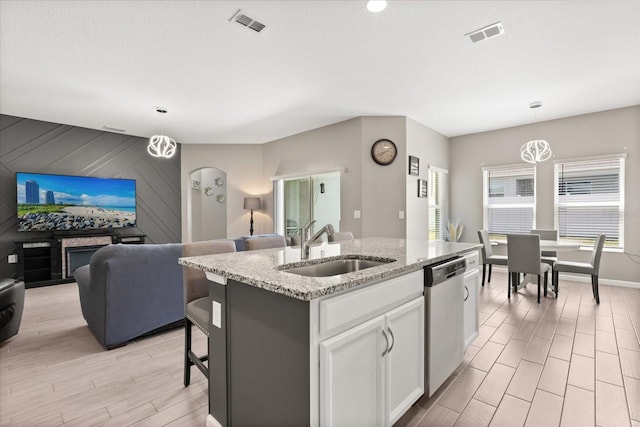 kitchen with open floor plan, stainless steel dishwasher, a center island with sink, a sink, and white cabinets