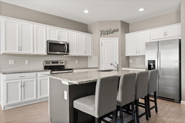 kitchen featuring white cabinetry, a center island with sink, a sink, light stone counters, and appliances with stainless steel finishes
