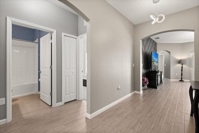 hallway featuring arched walkways, baseboards, and light wood-style floors