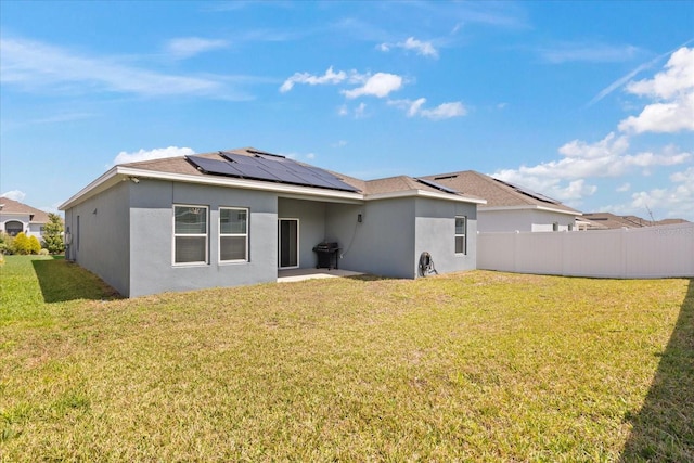 back of property featuring stucco siding, fence, roof mounted solar panels, and a yard