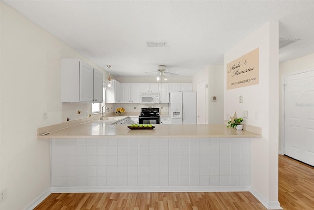 kitchen with light countertops, a sink, a peninsula, and white appliances