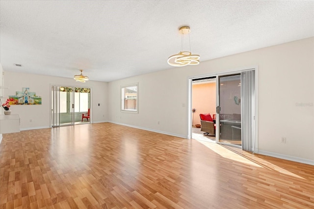 interior space with baseboards, a textured ceiling, light wood-style floors, visible vents, and a notable chandelier