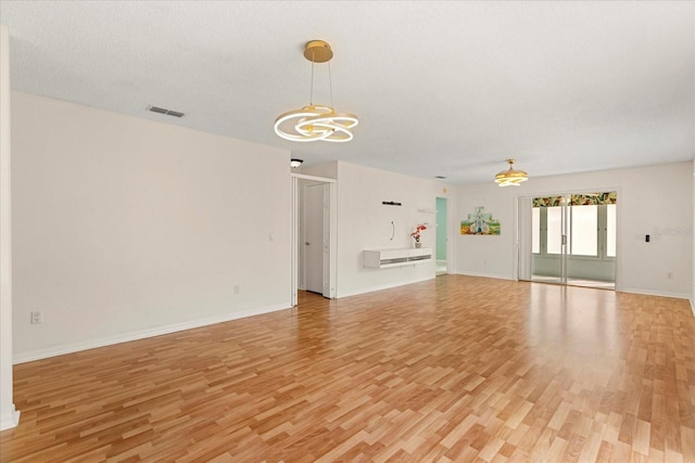 unfurnished living room with a chandelier, a textured ceiling, light wood-style flooring, baseboards, and visible vents