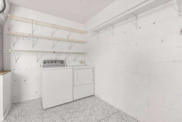 clothes washing area with concrete block wall, washing machine and dryer, and laundry area