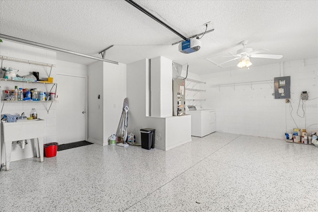 garage featuring concrete block wall, washing machine and clothes dryer, a garage door opener, a ceiling fan, and electric panel