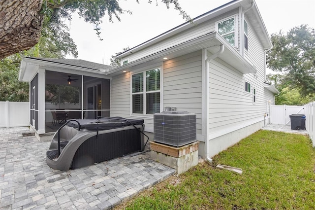 back of house with cooling unit, a sunroom, a hot tub, a patio, and a fenced backyard