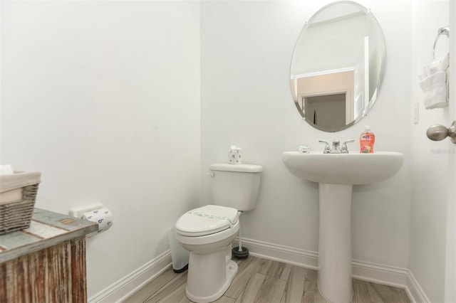 bathroom featuring toilet, a sink, baseboards, and wood finished floors