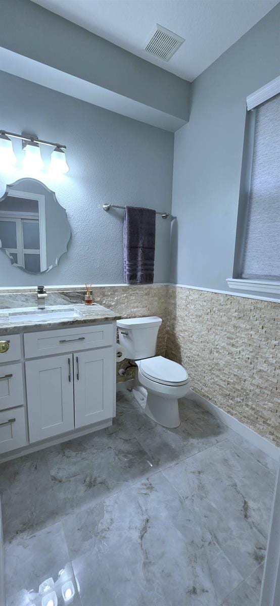 4730 Capital Blvd, Saint Cloud, FL 34769 - bathroom featuring tile walls, visible vents, toilet, vanity, and wainscoting
