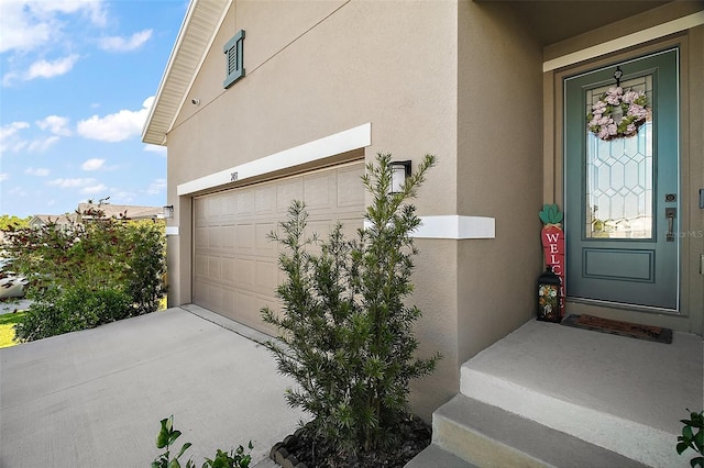 doorway to property featuring a garage, driveway, and stucco siding