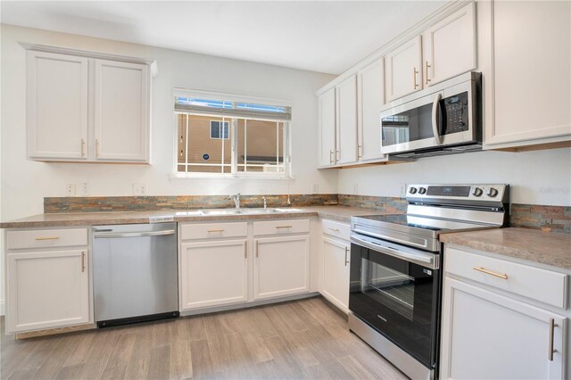 10124 Shadow Leaf Ct, Orlando, FL 32825 - kitchen featuring a sink, white cabinets, light wood-style flooring, and appliances with stainless steel finishes