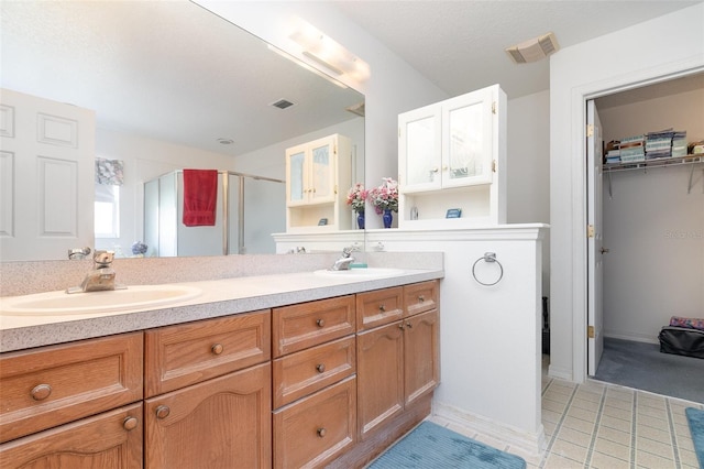 full bath with a stall shower, double vanity, visible vents, and a sink