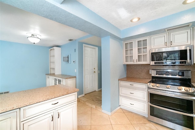 690 S Lakemont Ave, Winter Park, FL 32792 - kitchen featuring stainless steel appliances, glass insert cabinets, light tile patterned floors, and tasteful backsplash