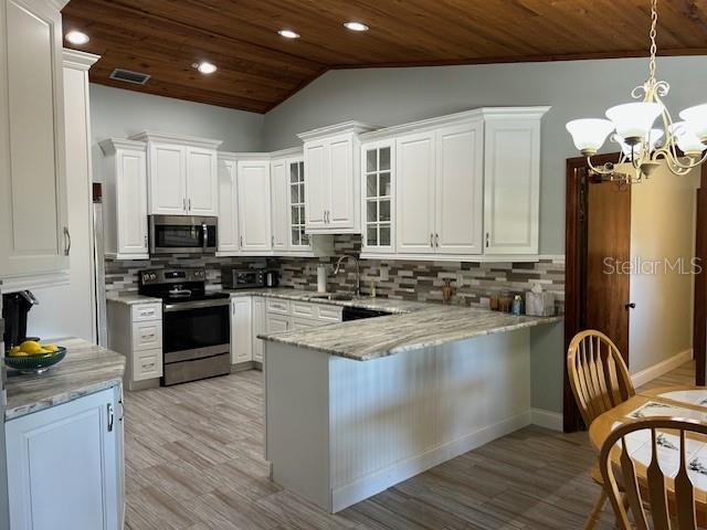 1500 Markham Woods Rd, Longwood, FL 32779 - kitchen with a chandelier, a peninsula, appliances with stainless steel finishes, white cabinetry, and wooden ceiling