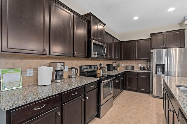 kitchen featuring tasteful backsplash, light tile patterned floors, light stone countertops, dark brown cabinets, and appliances with stainless steel finishes