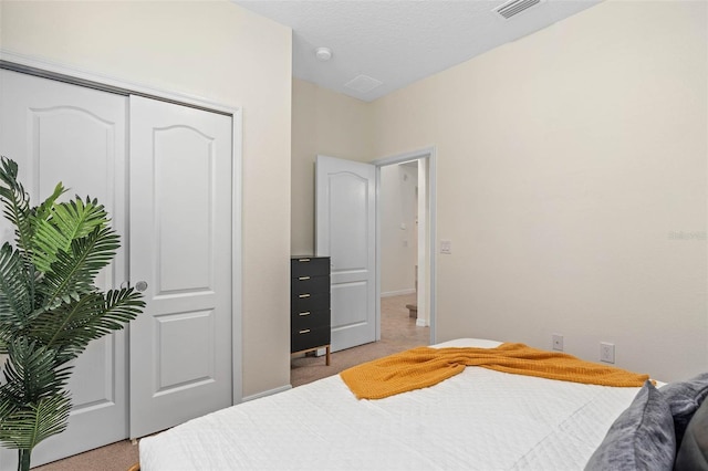 bedroom with a closet, light carpet, a textured ceiling, baseboards, and visible vents