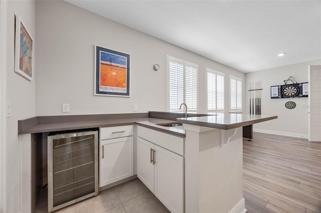 2011 Soaring Oak Way, Winter Park, FL 32792 - kitchen featuring a sink, a peninsula, white cabinetry, beverage cooler, and baseboards