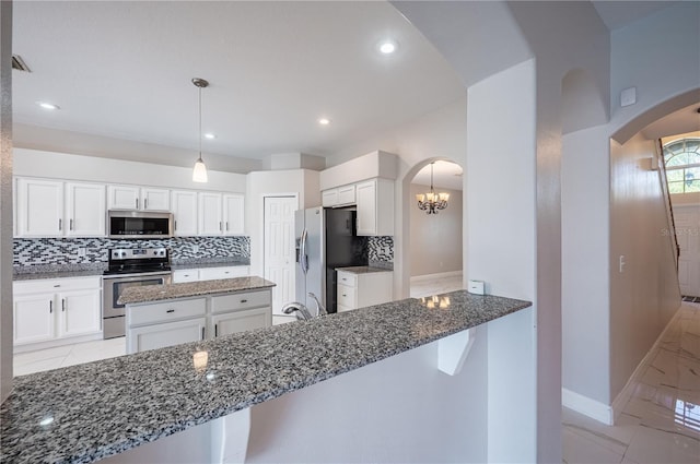 31028 Baclan Dr, Wesley Chapel, FL 33545 - kitchen featuring dark stone counters, stainless steel appliances, arched walkways, and decorative backsplash
