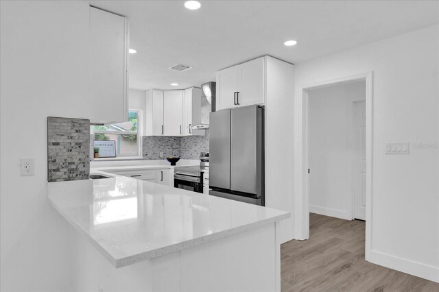 kitchen featuring visible vents, white cabinets, wall chimney exhaust hood, a peninsula, and stainless steel appliances