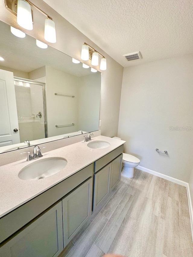 2834 Narcoossee Commons Way, Saint Cloud, FL 34771 - bathroom featuring wood finished floors, a shower stall, toilet, double vanity, and a textured ceiling