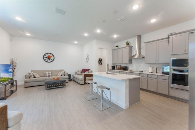 kitchen featuring gray cabinetry, a sink, wall chimney exhaust hood, and stainless steel oven