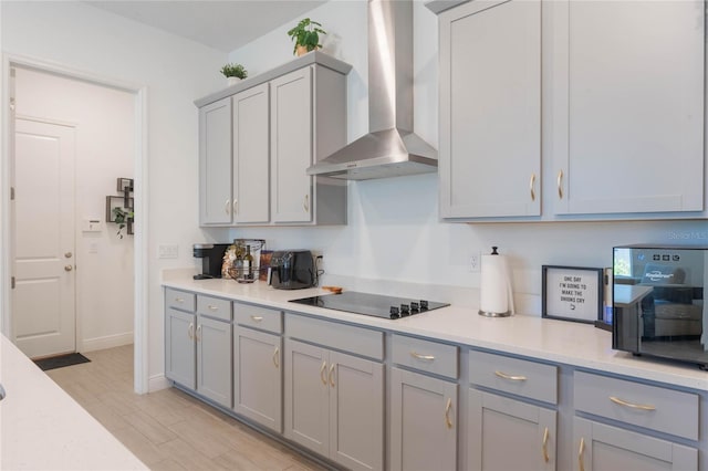 kitchen with light countertops, wall chimney range hood, light wood-style floors, black appliances, and gray cabinets