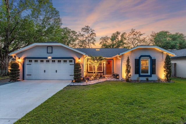ranch-style house featuring stucco siding, an attached garage, a yard, and driveway