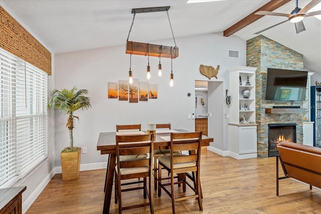 dining space with ceiling fan, a stone fireplace, light wood-style flooring, high vaulted ceiling, and baseboards