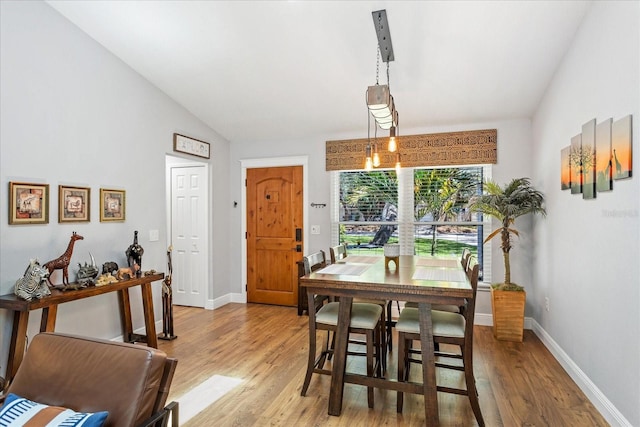 dining area featuring light wood finished floors, baseboards, and vaulted ceiling